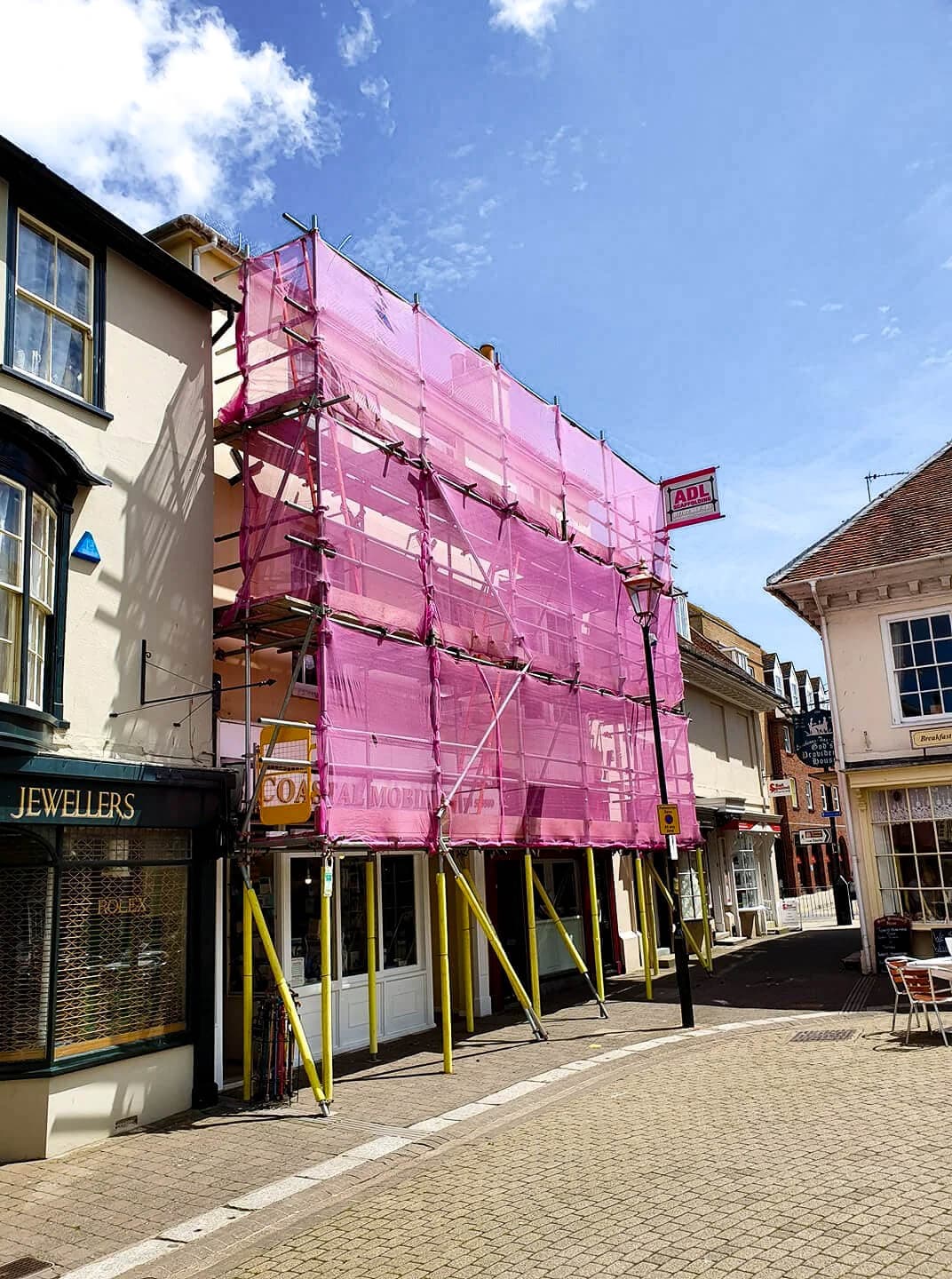 Town centre shop front with full pink scaffold netting in a pedestrian area, Isle of Wight